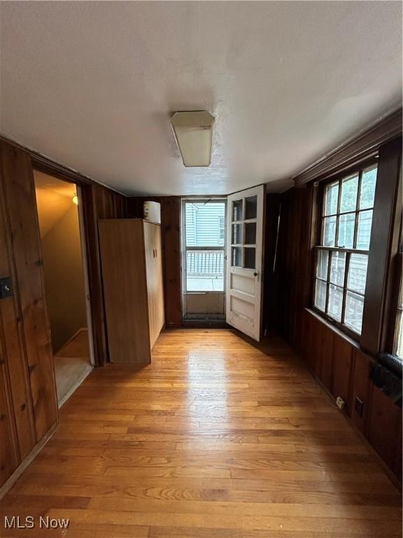 empty room featuring a textured ceiling, light wood-type flooring, and wooden walls