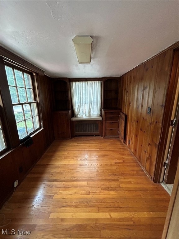 spare room featuring light wood-type flooring, wood walls, and radiator heating unit