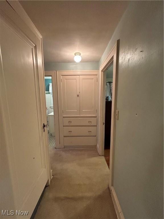 hallway with baseboards and light colored carpet