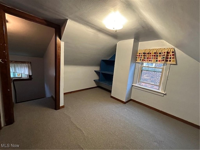 bonus room featuring lofted ceiling, a textured ceiling, carpet flooring, and baseboards