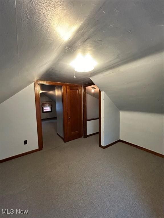 bonus room featuring a textured ceiling, light carpet, lofted ceiling, and baseboards