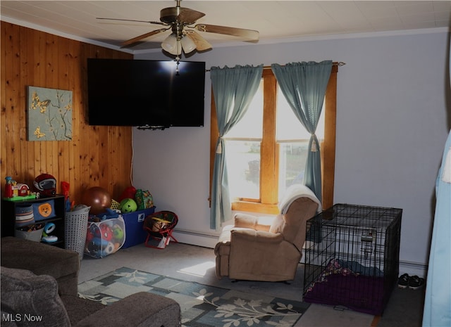 carpeted living room featuring a baseboard heating unit, crown molding, wood walls, and ceiling fan