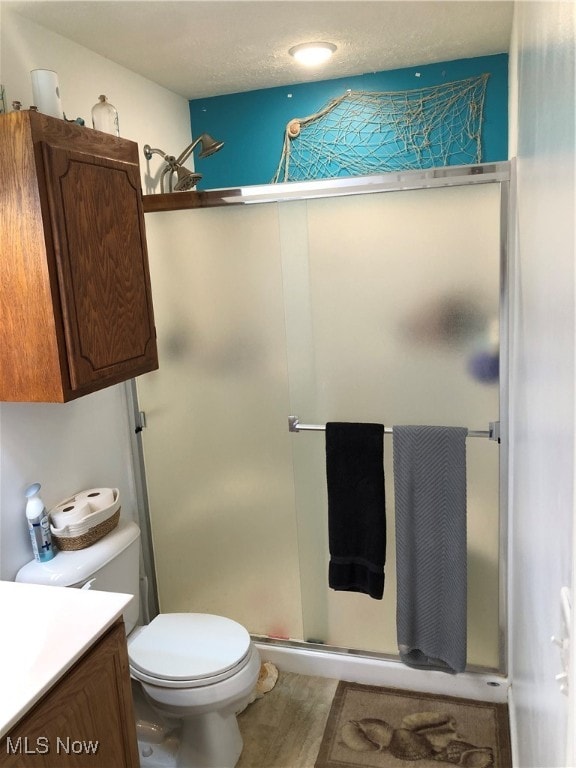 bathroom with vanity, toilet, a shower with shower door, and a textured ceiling