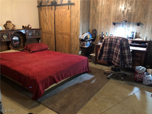 bedroom featuring a barn door, concrete flooring, and wooden walls