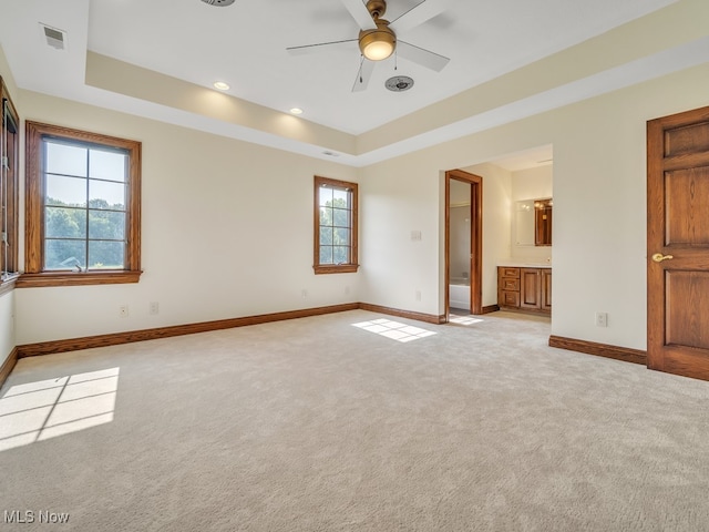 unfurnished bedroom with light colored carpet, a raised ceiling, ensuite bathroom, and ceiling fan