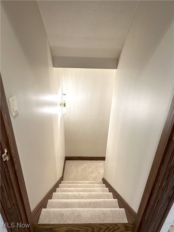 stairway with a textured ceiling, carpet flooring, and baseboards