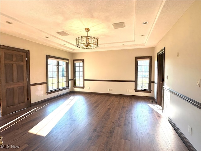 spare room featuring baseboards, dark wood-style flooring, a raised ceiling, and an inviting chandelier