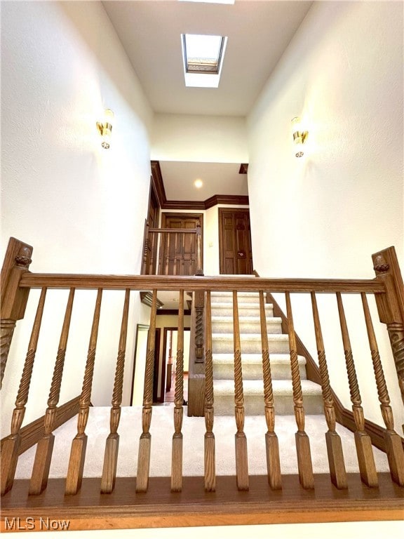 stairs featuring crown molding, carpet floors, and a skylight