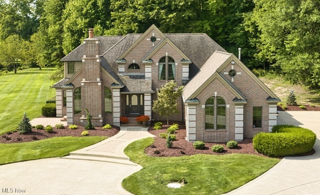 view of front of property featuring a shingled roof, a chimney, a front lawn, and brick siding