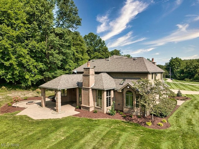 back of property featuring a patio, brick siding, a yard, roof with shingles, and a chimney