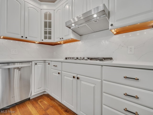 kitchen featuring backsplash, stainless steel appliances, ventilation hood, light wood-type flooring, and white cabinets