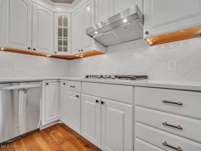 kitchen with light wood-style flooring, stainless steel dishwasher, glass insert cabinets, white cabinetry, and wall chimney exhaust hood