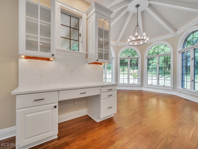 unfurnished office featuring a chandelier, built in desk, wood-type flooring, and vaulted ceiling with beams