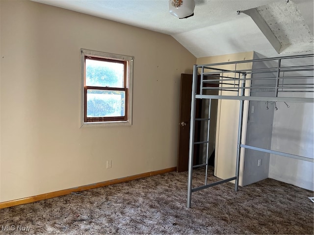 unfurnished bedroom with carpet floors, lofted ceiling, a textured ceiling, and baseboards