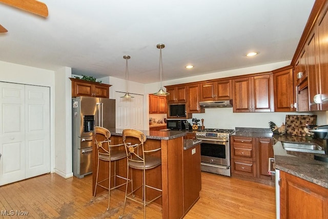 kitchen featuring light wood-type flooring, premium appliances, dark stone countertops, a kitchen island, and hanging light fixtures