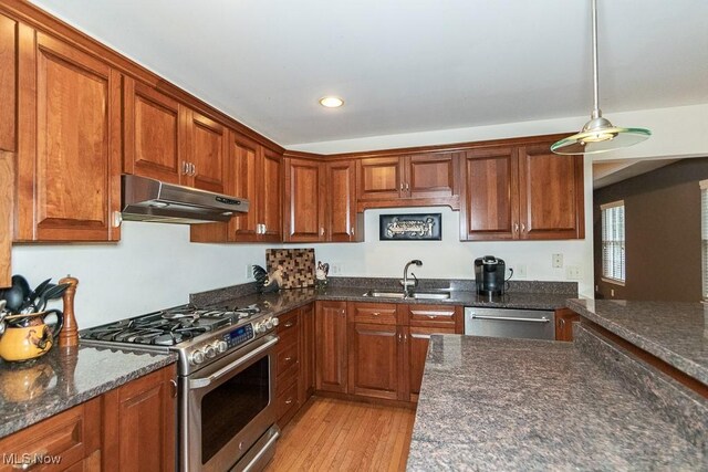 kitchen featuring appliances with stainless steel finishes, light hardwood / wood-style floors, dark stone countertops, and sink