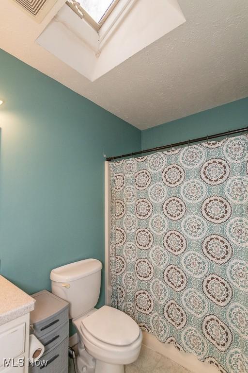 bathroom featuring walk in shower, tile patterned flooring, a textured ceiling, toilet, and vanity