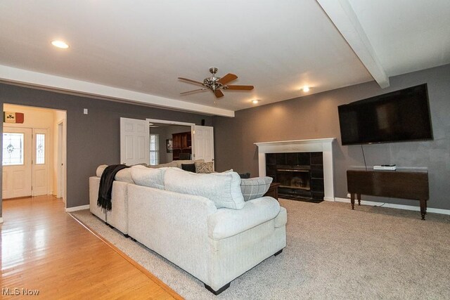 living room featuring ceiling fan, beam ceiling, and a tile fireplace