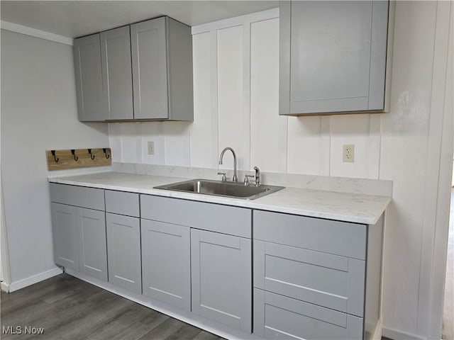 kitchen with a sink, light stone counters, gray cabinetry, and dark wood-style flooring