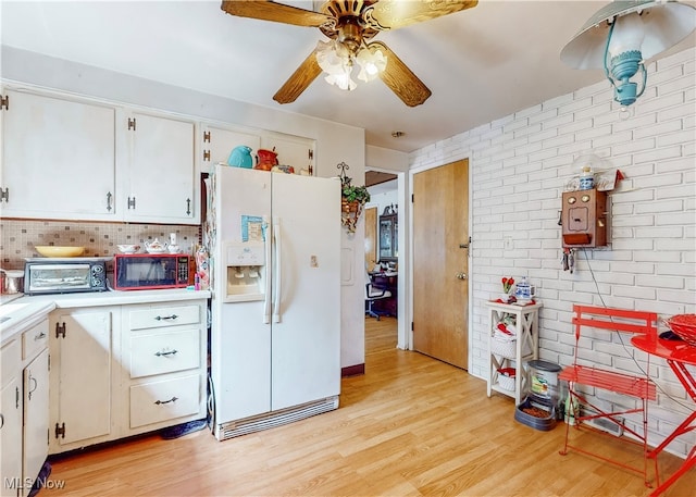 kitchen with light hardwood / wood-style flooring, white refrigerator with ice dispenser, white cabinetry, brick wall, and ceiling fan