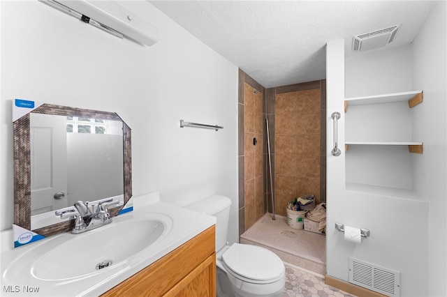 bathroom with tiled shower, vanity, toilet, and a textured ceiling