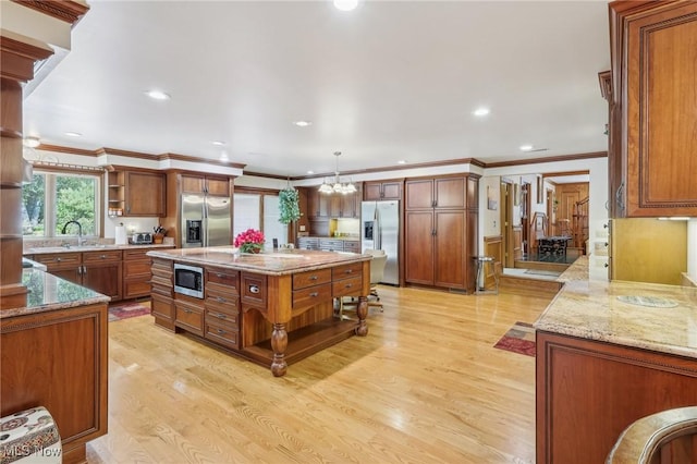 kitchen featuring decorative light fixtures, a center island, stainless steel appliances, light stone countertops, and light hardwood / wood-style floors