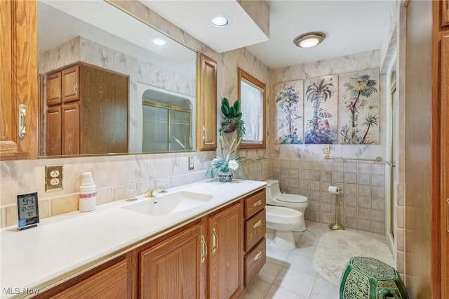 bathroom with a shower with shower door, tile walls, vanity, toilet, and a bidet