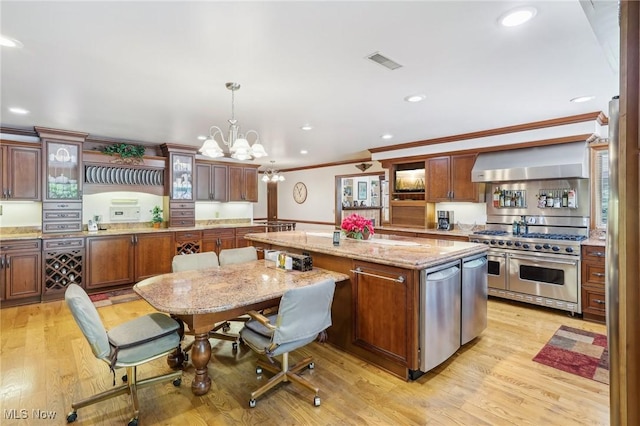 kitchen with hanging light fixtures, double oven range, a center island, light stone countertops, and wall chimney range hood