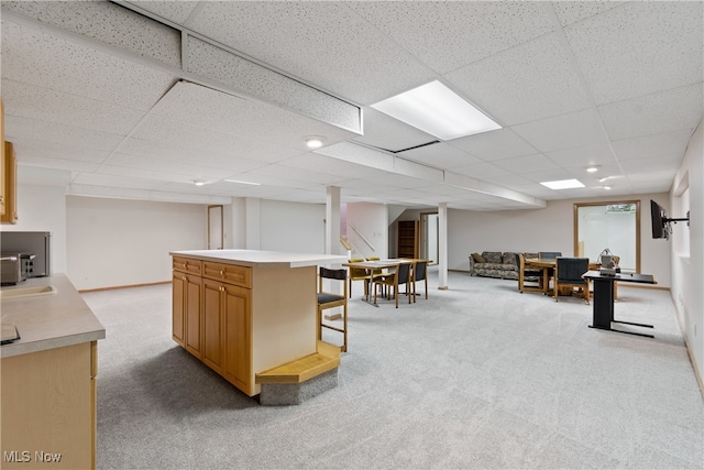 interior space with a breakfast bar area, light carpet, a center island, and a drop ceiling