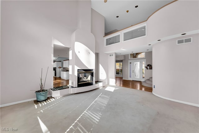 unfurnished living room with a multi sided fireplace, french doors, a towering ceiling, and carpet floors