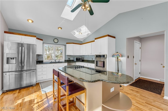 kitchen featuring white cabinetry, lofted ceiling with skylight, light hardwood / wood-style flooring, and stainless steel appliances