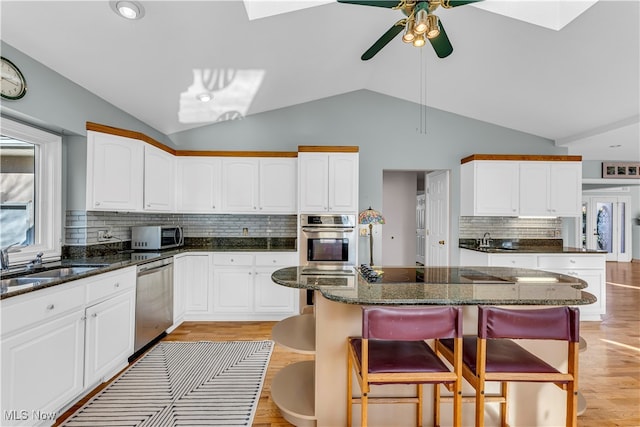 kitchen with appliances with stainless steel finishes, vaulted ceiling with skylight, sink, light hardwood / wood-style floors, and white cabinetry