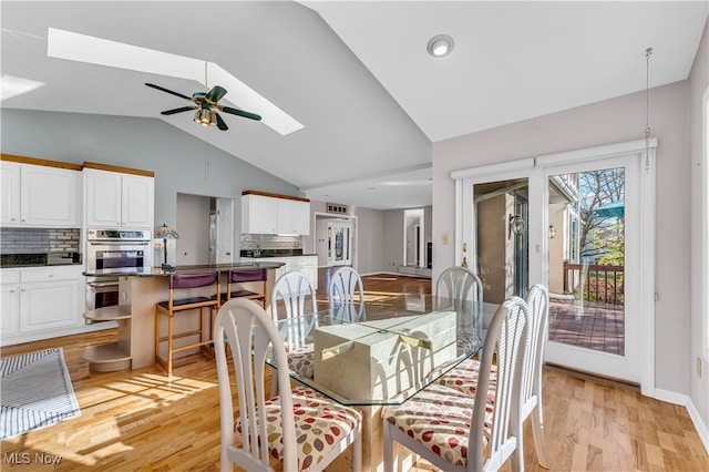 dining room featuring lofted ceiling with skylight, ceiling fan, and light wood-type flooring