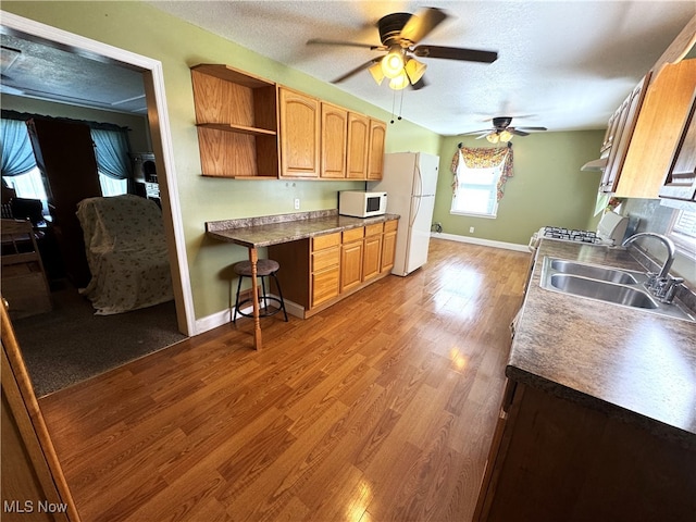 kitchen with hardwood / wood-style floors, white appliances, sink, ceiling fan, and a textured ceiling