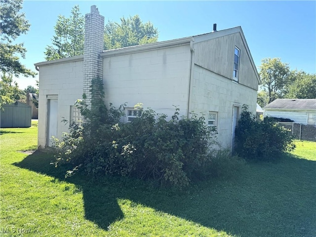 view of property exterior featuring a yard, a chimney, concrete block siding, and fence