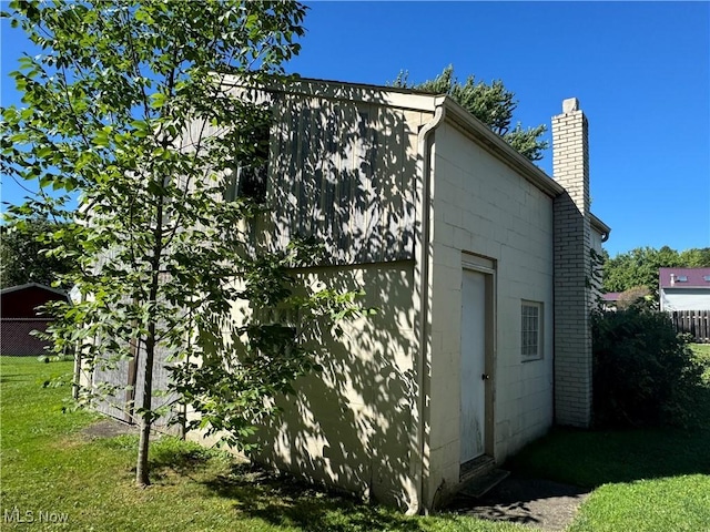 view of home's exterior with concrete block siding, a chimney, fence, and a yard