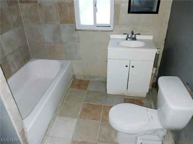 bathroom with vanity, toilet, a bathing tub, and tile walls