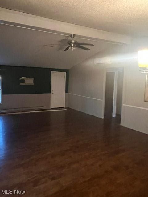 unfurnished living room featuring vaulted ceiling with beams, dark wood-type flooring, a textured ceiling, and a ceiling fan