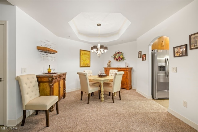 dining space with light colored carpet, an inviting chandelier, and a raised ceiling