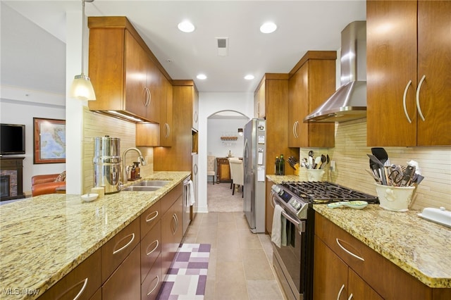 kitchen featuring tasteful backsplash, decorative light fixtures, stainless steel appliances, sink, and wall chimney range hood