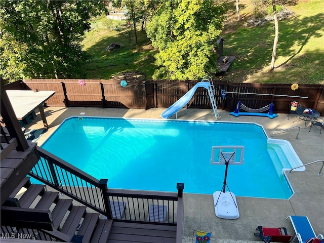 view of pool with a wooden deck, a lawn, and a water slide