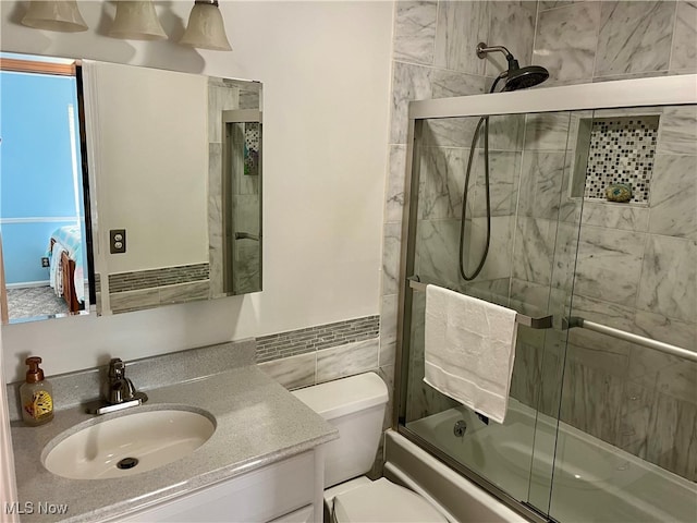 full bathroom featuring shower / bath combination with glass door, toilet, tile walls, and vanity