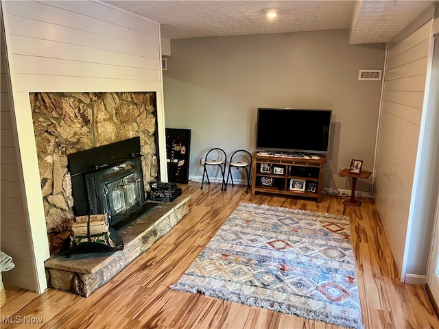 living room with a textured ceiling, a stone fireplace, and light hardwood / wood-style floors