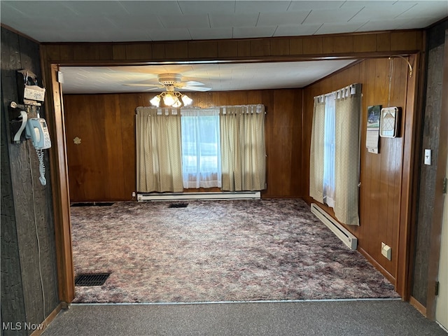 empty room with baseboard heating, carpet, ceiling fan, and wood walls