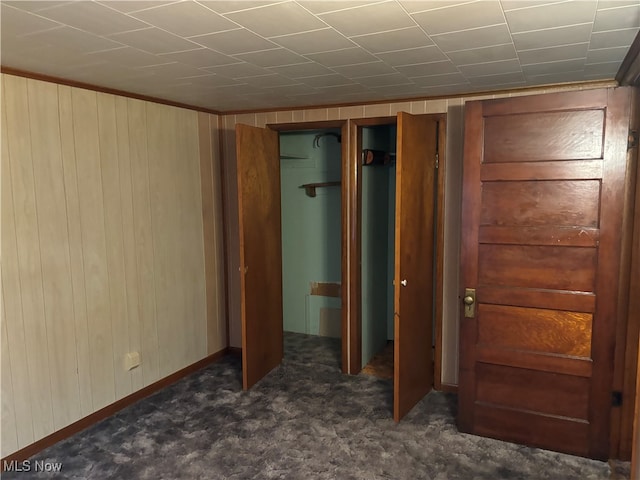 unfurnished bedroom featuring dark colored carpet and wooden walls