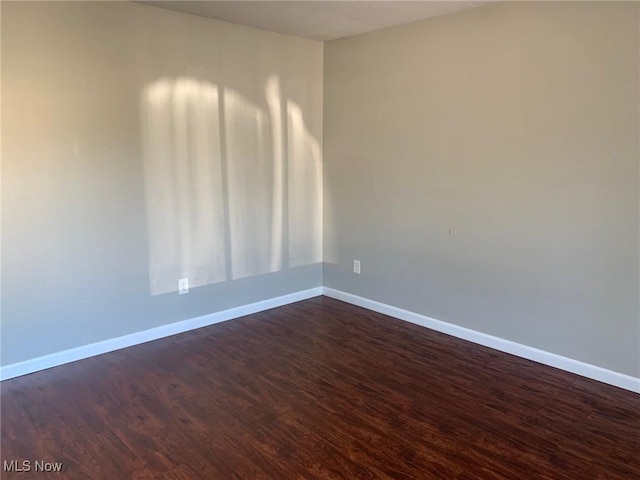 unfurnished room with baseboards and dark wood finished floors