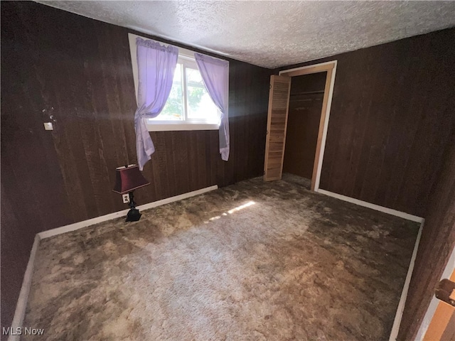 unfurnished bedroom with a closet, a textured ceiling, wood walls, and carpet floors