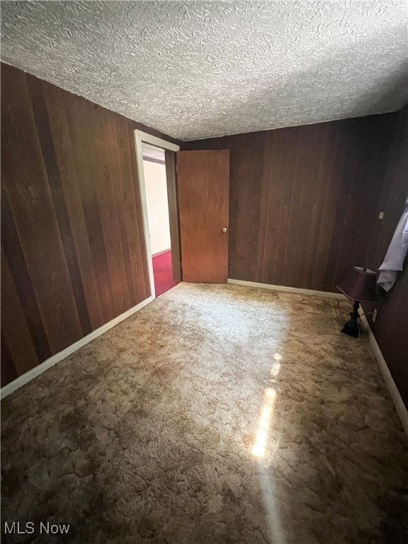 unfurnished room with a textured ceiling, carpet, and wooden walls