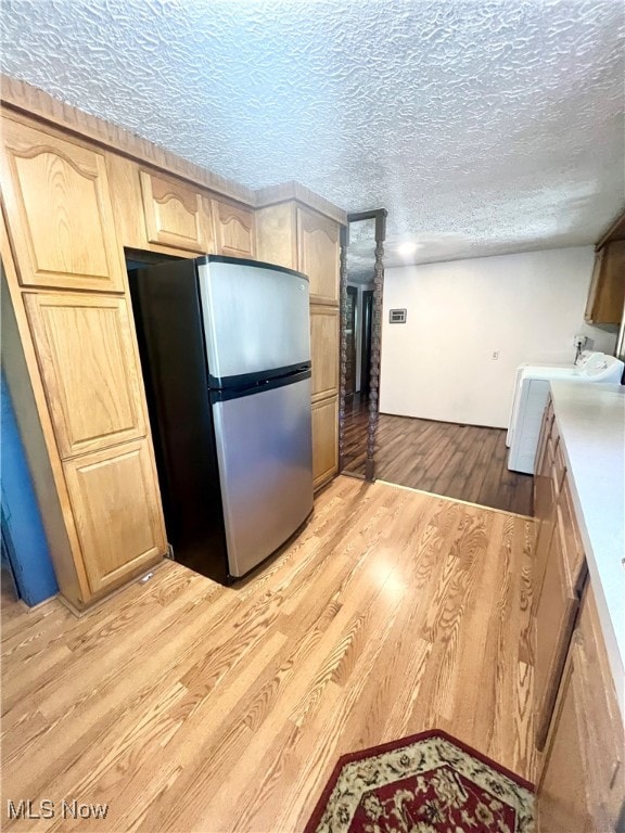 kitchen featuring a textured ceiling, stainless steel fridge, washer / dryer, light brown cabinets, and light wood-type flooring