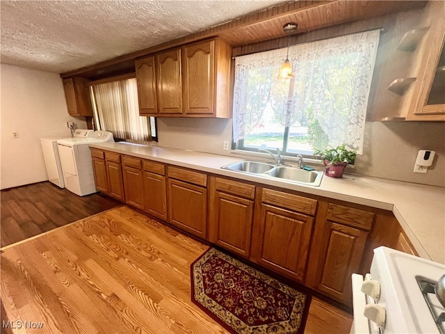 kitchen featuring independent washer and dryer, a textured ceiling, light hardwood / wood-style flooring, decorative light fixtures, and sink